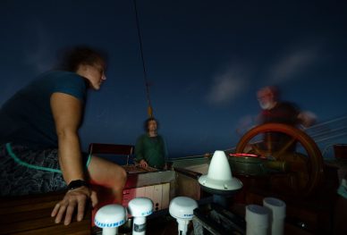 Three people steering a tall ship in the dark