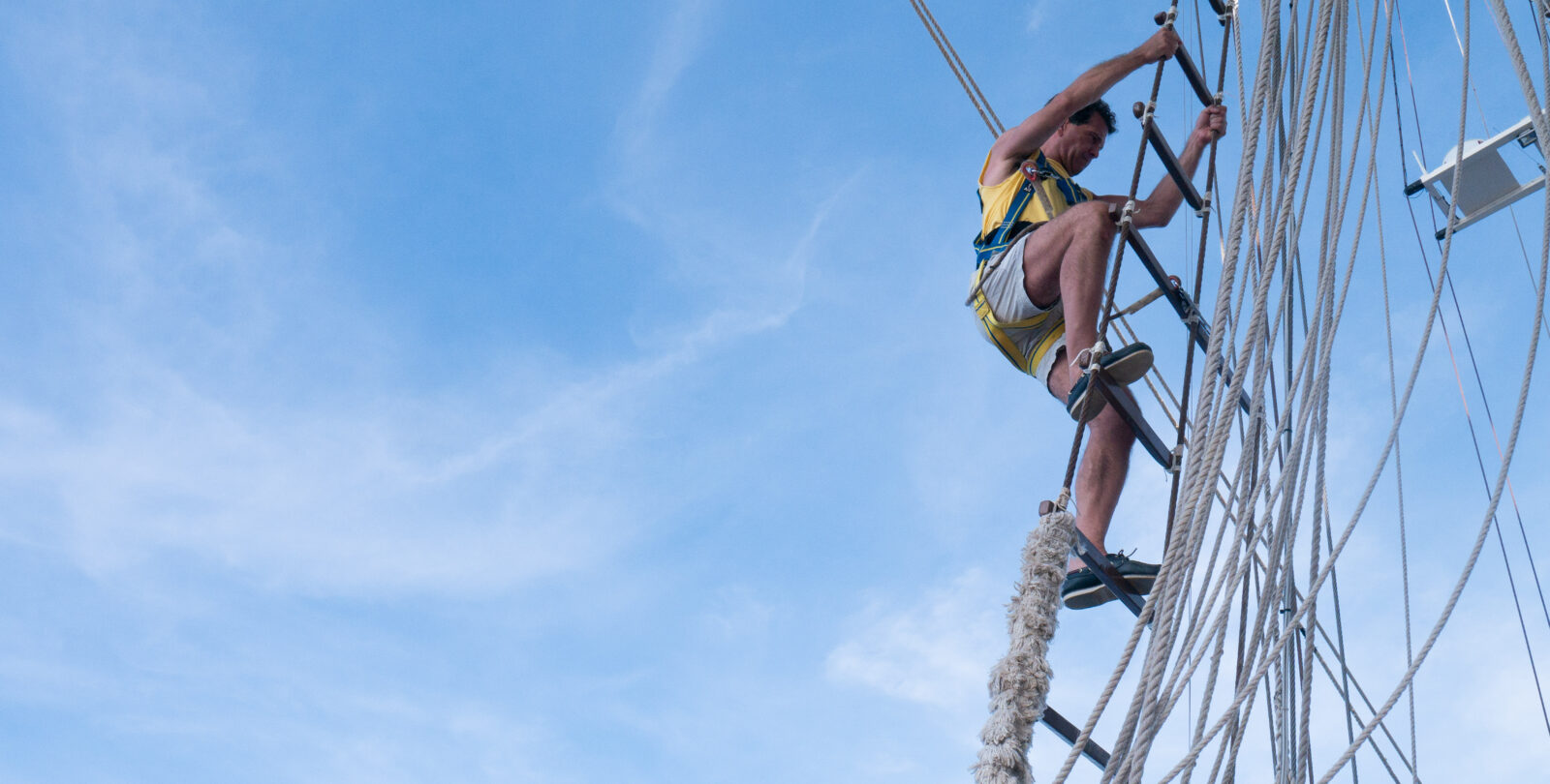 A man Climbs the rigging against a blue sky